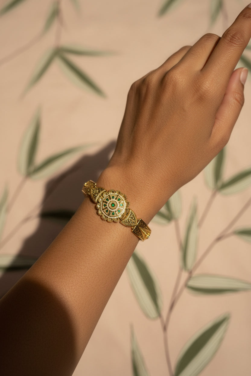 Gold bracelet with green gemstone on a leaf-patterned fabric background