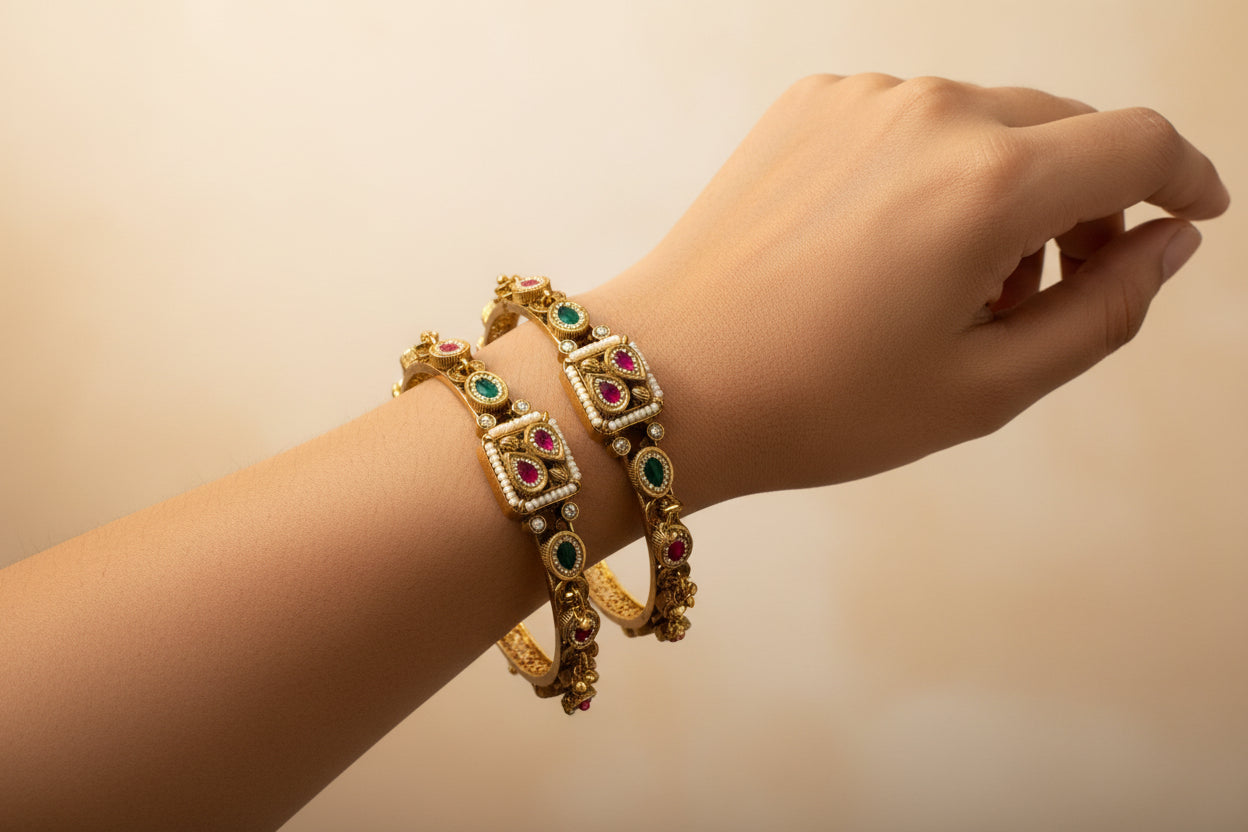 Hand wearing two gold bracelets with gemstones on a beige background